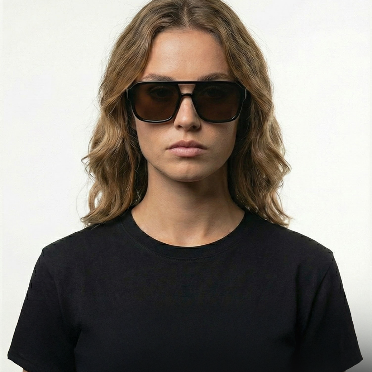 Model Ambine wears amber pilot sunglasses with black frames and dark lenses.