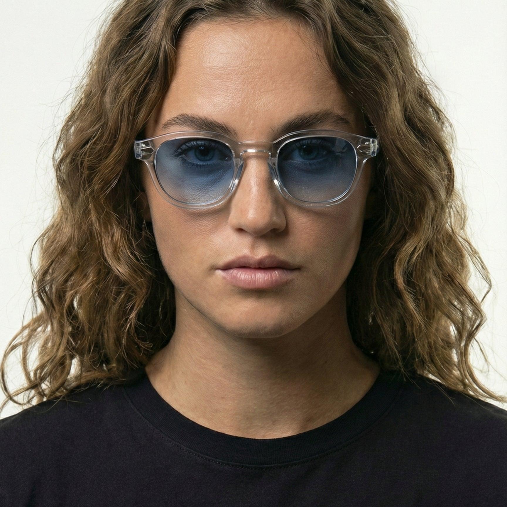 Model wearing Blue Clarity transparent frame sunglasses with blue gradient lenses.